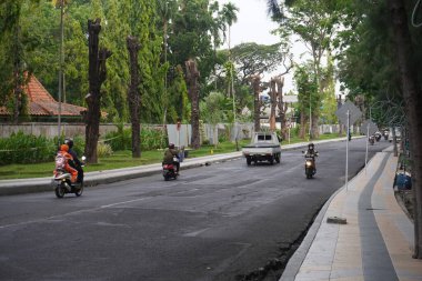 Motorists passing on a road surrounded by shady trees in the afternoon clipart