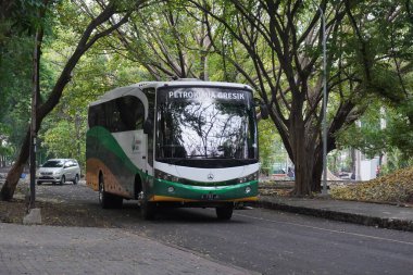 Öğleden sonra gölgeli ağaçların arasından geçen bir Petrokimia Gresik otobüsü