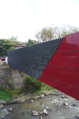 A red pedestrian bridge with grey lines connecting two areas separated by a river during the day clipart