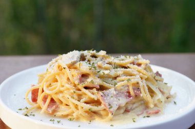 Beyaz yuvarlak bir tabakta servis edilen spagetti tabanlı makarna hazırlama servisi çekici bir görünüme ve bulanık bir arka plana sahip.