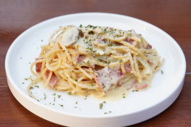 Beyaz yuvarlak bir tabakta servis edilen spagetti tabanlı makarna hazırlama servisi çekici bir görünüme ve bulanık bir arka plana sahip.