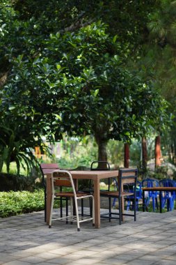 Gün boyunca açık bir kafede farklı şekillerde sandalyelerle çevrili açık bir tahta masa.