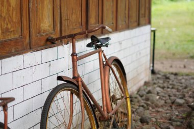 Gündüzleri beyaz tuğla ve tahtadan yapılmış bir evin duvarına yaslanmış antik altın bir bisiklet.