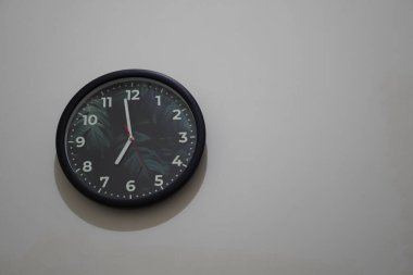 Beyaz bir arka planda saat 7 'de bir yaprağın resmini gösteren bir duvar saati.