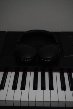 Dijital piyano tuşları hoparlörlerin üzerine yerleştirilmiş siyah kablosuz kulaklıklarla susturuluyor.