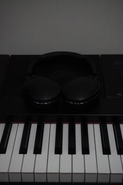Dijital piyano tuşları hoparlörlerin üzerine yerleştirilmiş siyah kablosuz kulaklıklarla susturuluyor.