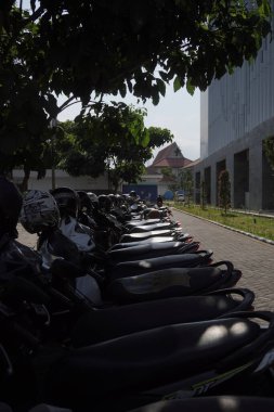 Kasklı motosikletler aynalara yerleştirilmiş ve düzgün bir şekilde büyük bir binanın kenarına park edilmiş.