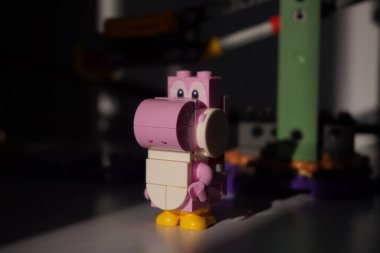  Lego pembe Yoshi minyatür figürü. Güneş ışığı ve bulanık arkaplan önünde çekilmiş.