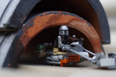 Lego minyatürleri Mandalorian ve Bebek Yoda (Grogu) bulanık bir arka plana sahip karanlık bir tünelden geçiyorlar.