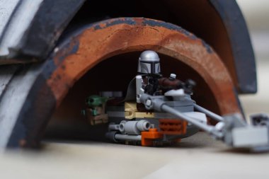 Lego minyatürleri Mandalorian ve Bebek Yoda (Grogu) bulanık bir arka plana sahip karanlık bir tünelden geçiyorlar.
