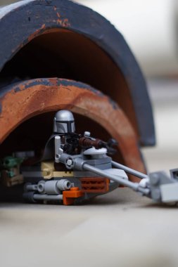 Lego minyatürleri Mandalorian ve Bebek Yoda (Grogu) bulanık bir arka plana sahip karanlık bir tünelden geçiyorlar.