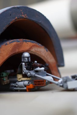 Lego minyatürleri Mandalorian ve Bebek Yoda (Grogu) bulanık bir arka plana sahip karanlık bir tünelden geçiyorlar.