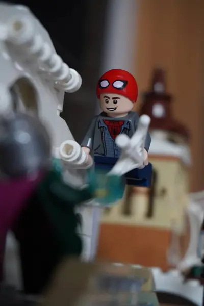 stock image Minifigure Peter Parker (Spider Man) with a half-open mask is hanging on the bridge fighting Mysterio