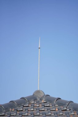 Arka plan olarak mavi gökyüzü olan bir evin çatısına bir yıldırım koruma cihazı yerleştirildi.