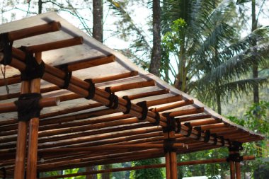 Plastik asbest ve ahşap direklerden yapılmış basit bir çatı. Ağaçlardan oluşan siyah bir halatla bağlanmış.