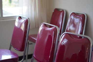 Red chairs lined up in a room during the day clipart