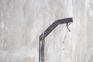 Gündüz vakti gri bir duvarın yanında açık kablolar olan kirli siyah bir direk.