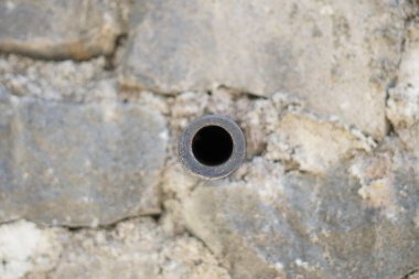 A small pipe in the middle of a wall made of piles of stones clipart