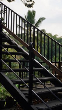 Siyah demir merdiven, uzun hindistan cevizi ağacı arka planlı endüstriyel bir konsepte sahiptir.