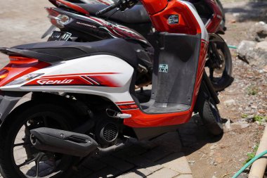 Kırmızı beyaz bir Honda Genio motosikleti park etmiş.