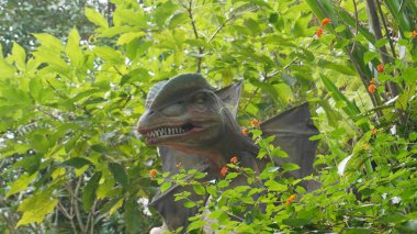 Ağaç yaprakları arasında fan benzeri kulakları olan bir dinozor heykeli. 