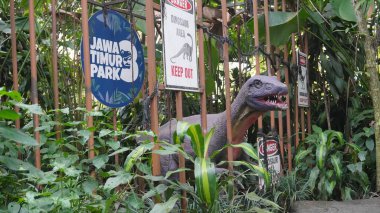 Dino Park Jatim Parkı 3 Batu 'da tehlikeli yazı ve orman geçmişi olan bir kafese kapatılmış dinozor heykeli.