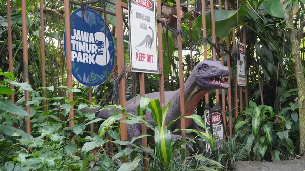 Stock image Dinosaur statue caged in a cage with dangerous writing and forest background at Dino Park Jatim Park 3 Batu