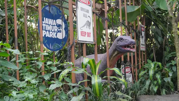 stock image Dinosaur statue caged in a cage with dangerous writing and forest background at Dino Park Jatim Park 3 Batu