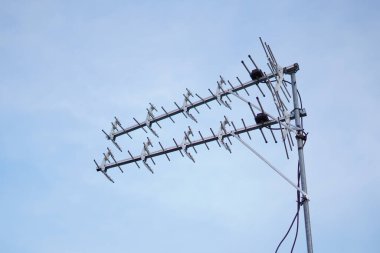 Mavi gökyüzü olan bir evin çatısına televizyon anteni yerleştirilmiş.