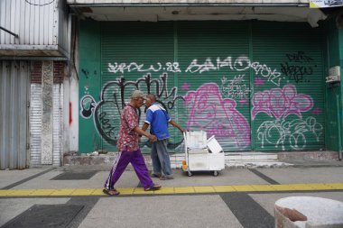 Yolun kenarındaki kapalı bir dükkanın önünde iki yaşlı adam zıt yönde yürüyordu.