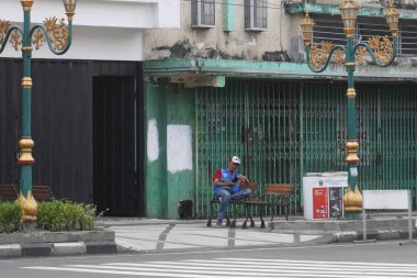 A parking attendant sitting alone on the sidewalk in Kayutangan, Malang clipart