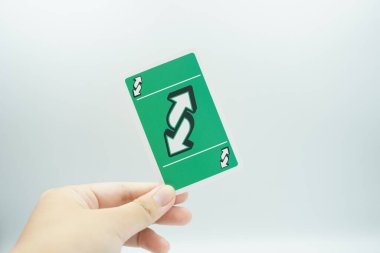 A hand holding a green reverse card from the UNO card game on a white background clipart