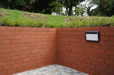 Arka plan kırmızı tuğla, yeşil çimen ve taş kaldırımlı ağaçlardan ve bahçe ışıklarından oluşuyor.