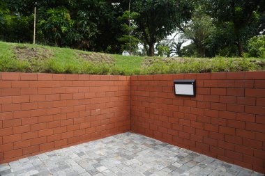 Arka plan kırmızı tuğla, yeşil çimen ve taş kaldırımlı ağaçlardan ve bahçe ışıklarından oluşuyor.