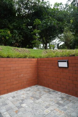 Arka plan kırmızı tuğla, yeşil çimen ve taş kaldırımlı ağaçlardan ve bahçe ışıklarından oluşuyor.