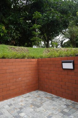 Arka plan kırmızı tuğla, yeşil çimen ve taş kaldırımlı ağaçlardan ve bahçe ışıklarından oluşuyor.