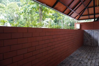 Kırmızı tuğlalar ve beton duvarlarla çevrili, kurumuş yapraklarla döşenmiş bir yer.