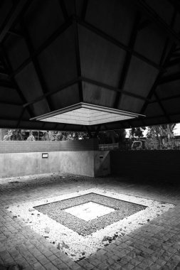 Ortadaki çatıda yarı açık bir bahçe var. Açık çatıdan siyah beyaz bir şekilde gelen güneş ışığına maruz kalmış bir kutu var.