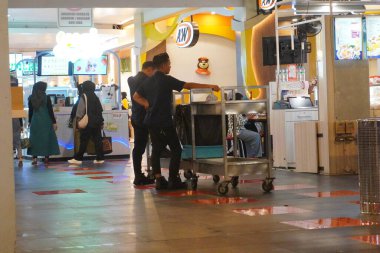 A cleaner at a mall's food court is carrying a push to clean dirty plates on the table. clipart