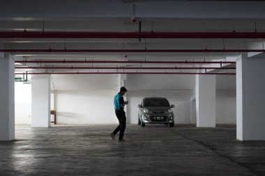 A man walking alone looking down at a deserted basement parking lot with one car clipart