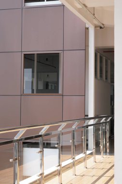 Minimalist kahverengi bir binanın balkon alanı sabah güneşine maruz kalan gümüş bir korkulukla çevrili.