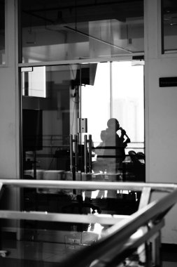 Arka planda uzun bir bina olan cam kapılı odalardan birinde konuşan bir kadının gölgesi.