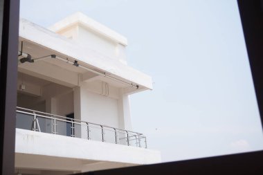Minimalist, beyaz, çok katlı bir binanın balkonunda alt pencereden görüldü.