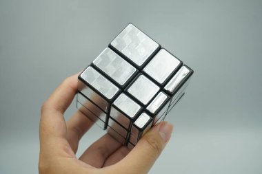 Sol elde beyaz arka planda karıştırılmamış 3x3 gümüş rubik ayna küpü var.