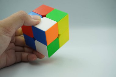 Sol el 2x2 Rubik 'in oyuncağını tutuyor. Beyaz bir arka planı var.
