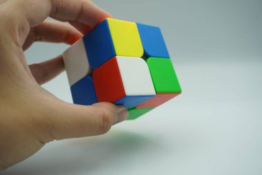 Sol el 2x2 Rubik 'in oyuncağını tutuyor. Beyaz bir arka planı var.
