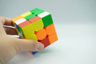 The left hand holds a 3x3 rubik that is scrambled on a white background clipart