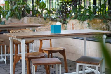 Minimalist ahşap bir masa ve bir kafede hiç kimse oturmadan ortada mavi bir mendil tutacağı olan sandalyeler.