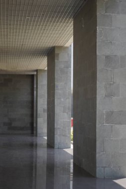 Gri sütunları olan bir binada uzun bir koridor ve sütunların arasından gelen birkaç ışık huzmesi.