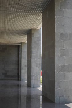 Gri sütunları olan bir binada uzun bir koridor ve sütunların arasından gelen birkaç ışık huzmesi.